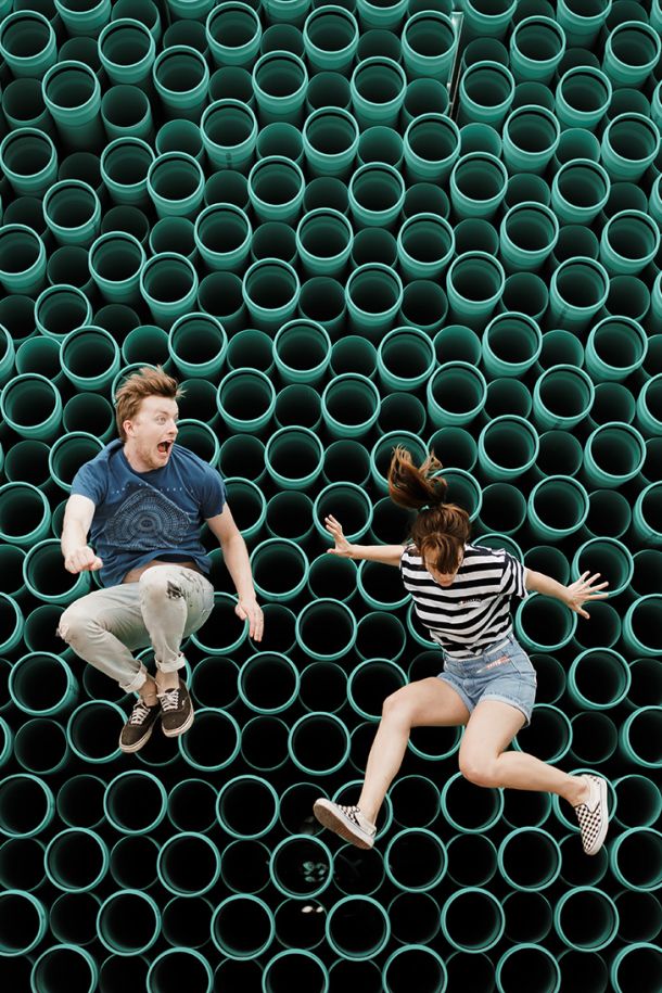 Two people jumping in front of a wall of green pipes, highlighting innovation, dynamic solutions, and team energy.