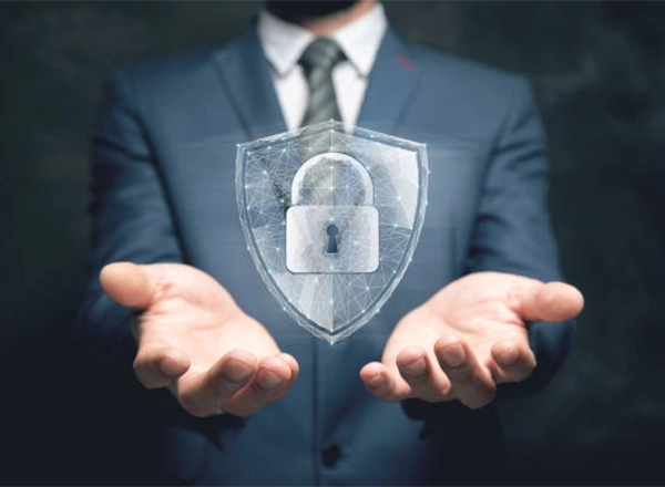 A person in a business suit is holding their hands out, palms up, with a glowing shield icon floating between them. The shield contains a padlock icon, symbolizing digital security and data protection.