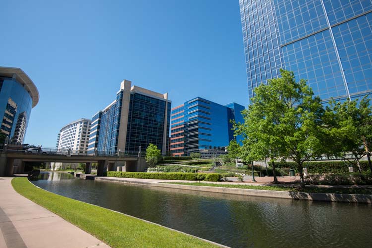 Modern office buildings and canal in The Woodlands, Texas, representing Elevate Technology’s local IT support, cybersecurity, and managed IT services for businesses in The Woodlands.