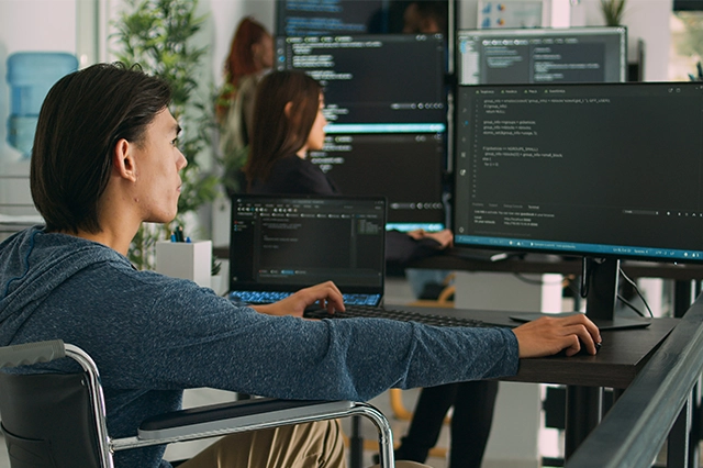 Team of IT professionals coding and monitoring software systems on multiple screens, representing cybersecurity, IT support, and managed services by Elevate Technology.