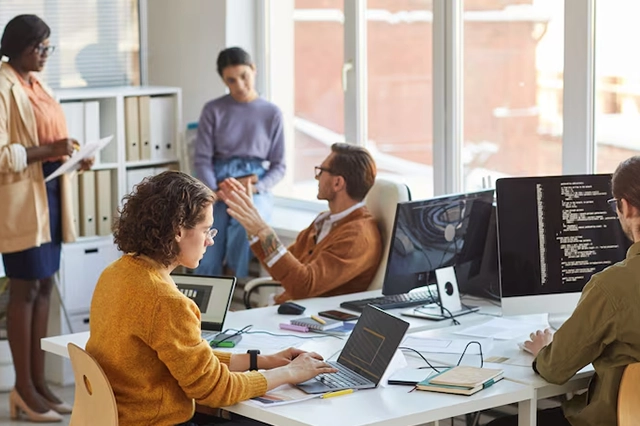 Team of IT professionals collaborating in a modern office, working on laptops and coding on desktop screens, showcasing teamwork, software development, and managed IT solutions by Elevate Technology.