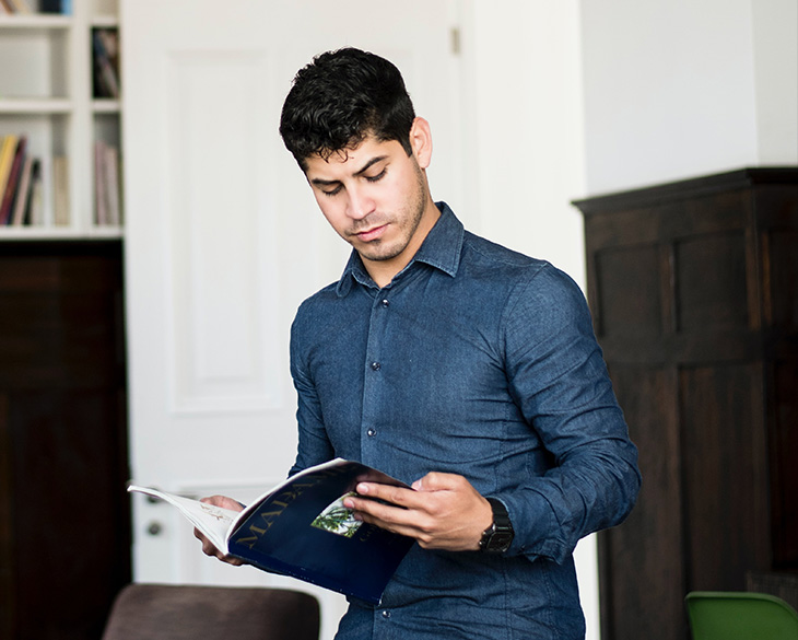 A focused Elevate Technology employee in a denim shirt stands indoors, reading a professional magazine or document.