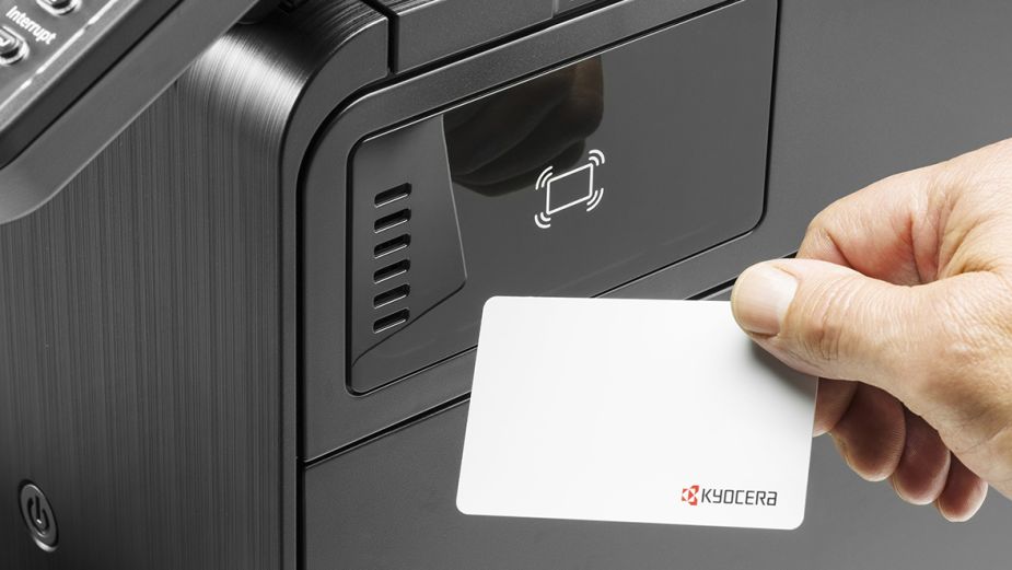A close-up of a hand using a Kyocera ID card to activate the card reader on a printer.