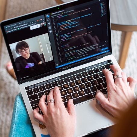 Developer's hands on a laptop keyboard during a video call, showcasing coding, cloud hosting, business email, and cloud email by Elevate Technology.