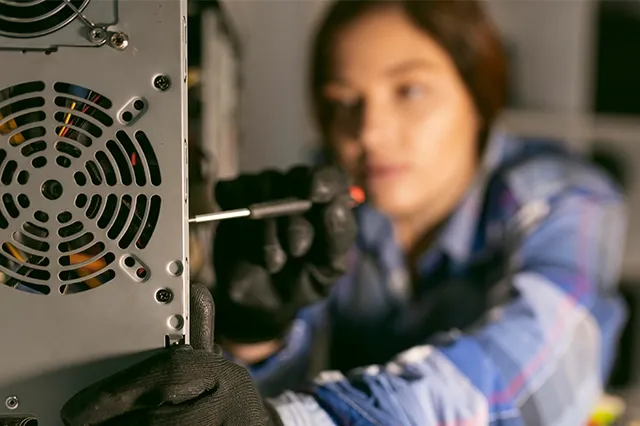 A professional woman wearing black gloves, using a screwdriver to service the internal components of a computer tower.
