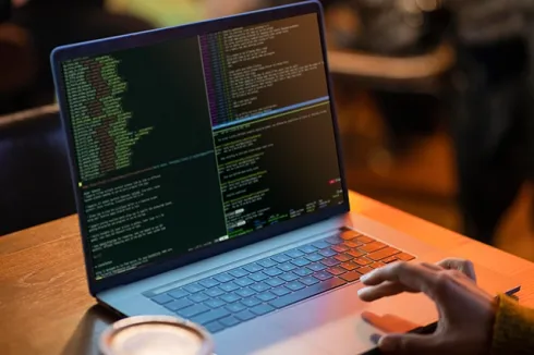 A laptop displaying code with a hand typing on the keyboard, highlighting programming, software development, and IT solutions.
