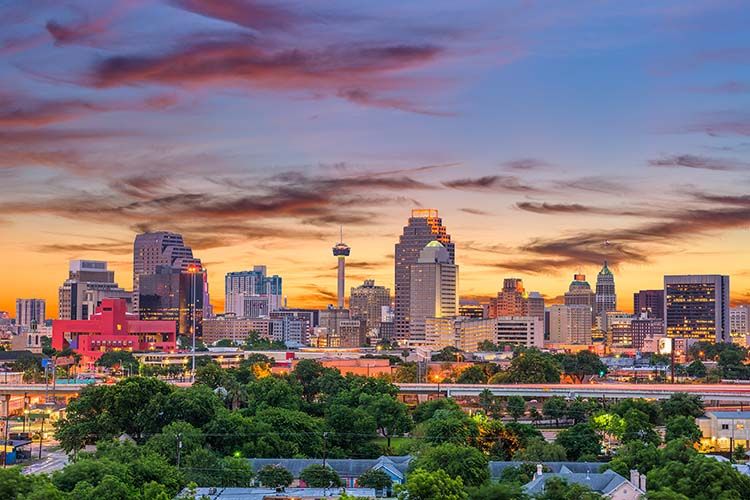 A wide-angle view of the San Antonio, Texas skyline at sunset, with the colorful sky behind the city's buildings and the Tower of the Americas prominently featured. This image is for Elevate Technology.