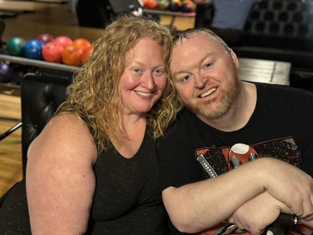 Elevate Technology close-up photo of a smiling woman and man, possibly team members, with bowling balls visible in the rack behind them.